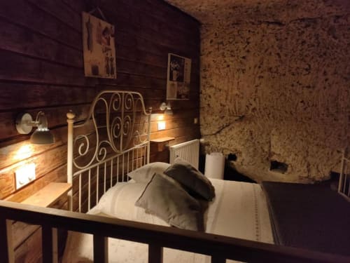 Cozy bedroom at Les Troglos de Beaulieu with ornate metal bed frame, cork walls, warm lighting, and classic furnishings