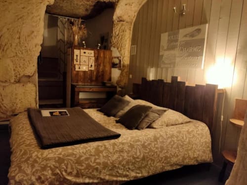 Rustic troglodyte bedroom at Les Troglos de Beaulieu with stone walls, wooden bed frame, and period furnishings in