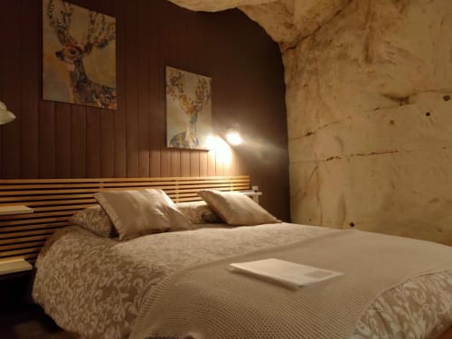 Chambre cosy aux Troglos de Beaulieu avec murs en pierre, tête de lit en bois et éclairage chaleureux à Beaulieu-les-Loches