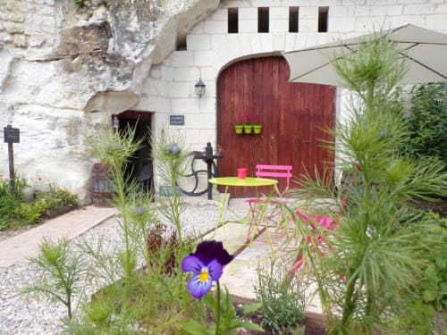 Charming garden courtyard at Les Troglos de Beaulieu with colorful furniture and purple pansies