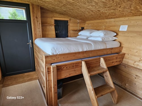 Chambre de refuge en bois avec lit surélevé, échelle, literie blanche et décor de chalet montagnard