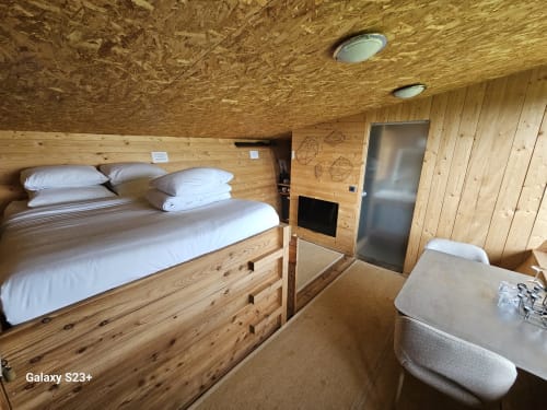Chambre douillette en bois au Logis Las Crozas avec lits jumeaux, draps blancs, éclairage encastré et porte métallique à Vernines