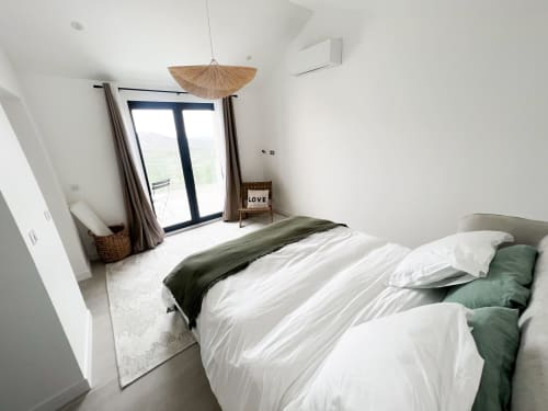 Chambre moderne à l'hôtel Anne Duval à Saint-Florent : linge blanc, accents verts, luminaire suspendu et accès balcon.
