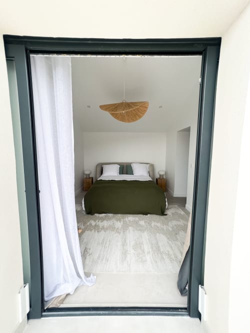 Chambre de l'hôtel Anne Duval à Saint-Florent avec literie verte, suspension en rotin et décoration minimaliste contemporaine