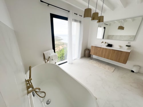 Salle de bain luxueuse de l'hôtel Anne Duval à Saint-Florent avec baignoire îlot, meuble vasque en bois et vue panoramique côtière