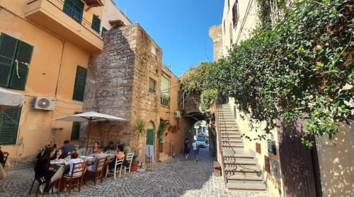 Area pranzi esterna nel cortile Nettuno con muri ricoperti di edera, edifici storici in pietra e ospiti che cenano sotto ombrelloni