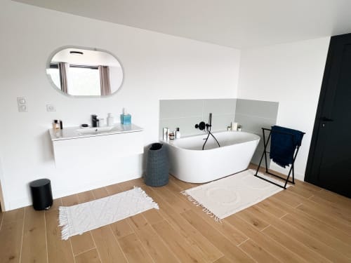 Salle de bain moderne de l'hôtel Anne Duval à Saint-Florent avec baignoire îlot blanche, miroir ovale et parquet