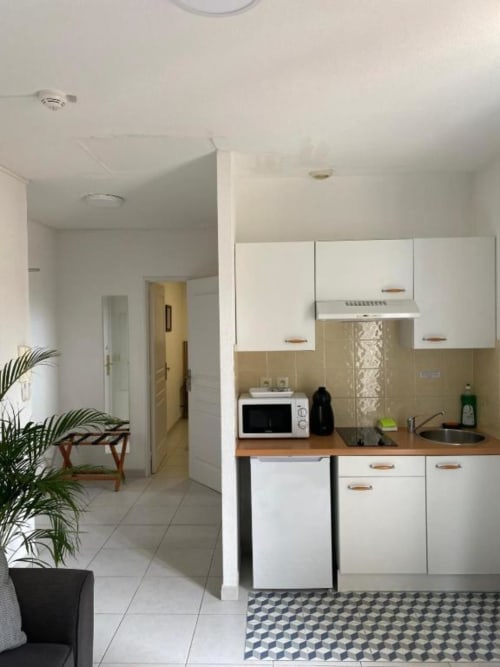 Kitchenette moderne à la Kimi Résidence à Cannes avec armoires blanches, plan de travail en bois, micro-ondes et carrelage géométrique