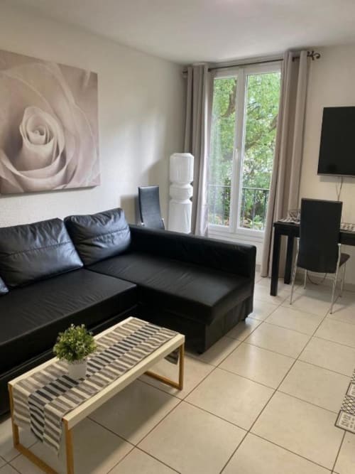 Séjour moderne à Kimi Résidence Cannes avec canapé noir, banquette rayée, tableau fleuri et vue sur le jardin