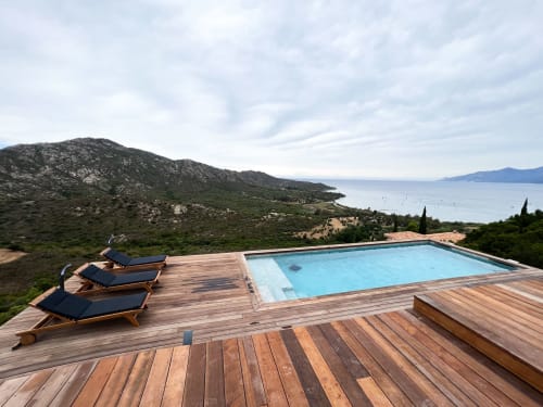 Piscine de l'hôtel Anne Duval dominant la baie de Saint-Florent avec terrasse en bois, transats et vue sur la côte méditerranéenne