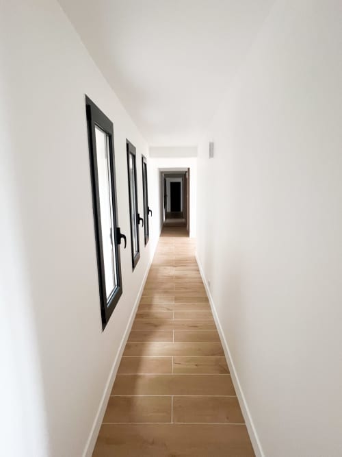 Couloir contemporain de l'hôtel Anne Duval à Saint Florent avec murs blancs, parquet et portes vitrées à encadrements noirs