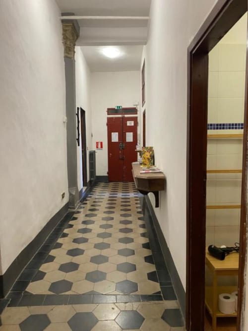 Hallway at Bronze Horse Affittacamere in Florence with geometric tile floor, red exit door, and open room entrance on right