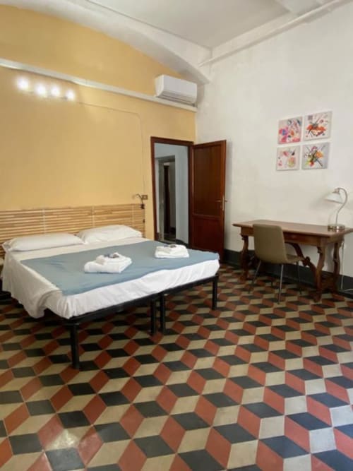 Amplia habitación en Bronze Horse Affittacamere en Florencia con paredes amarillas, cama de madera, escritorio y piso de azulejos geométricos.
