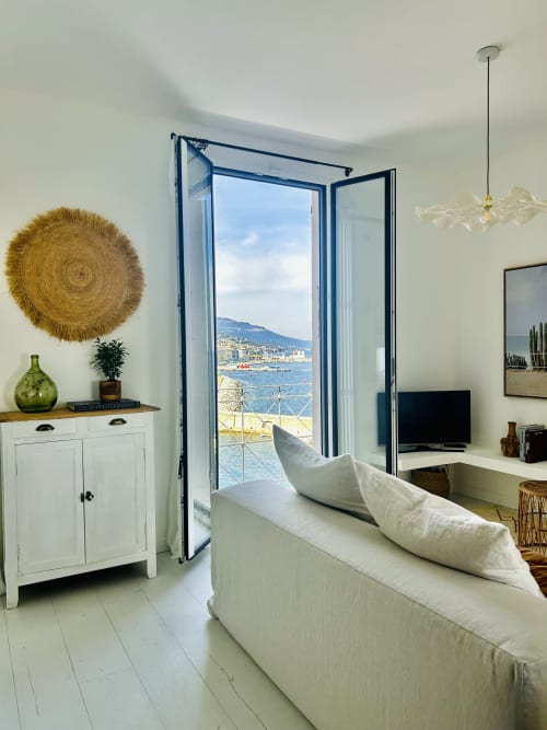 Bright Bastia apartment with coastal sea view through blue French doors, cream sofa, and white cabinetry