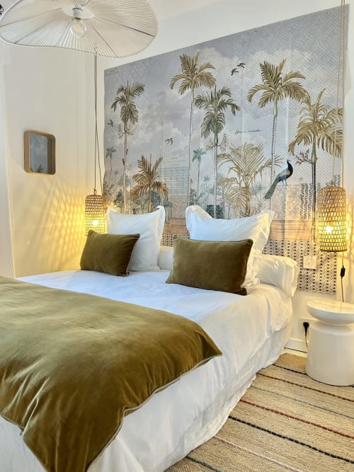 Tropical-themed bedroom at Casa di Bastia with palm tree wallpaper, olive bedding, woven pendant lights, and sea view balcony