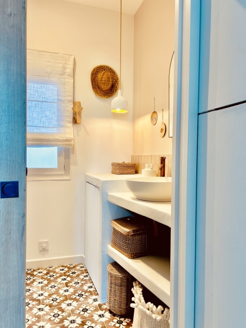 Modern bathroom in Casa di Bastia apartment with white sink, woven storage baskets, patterned floor tiles, and warm lighting
