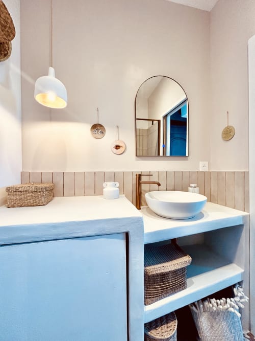 Modern bathroom at Casa di Bastia with blue vanity, white vessel sink, arched mirror, and woven storage baskets in Bastia,