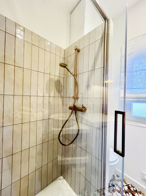 Modern shower enclosure with beige tiles and brass fixtures in Casa di Bastia apartment, Bastia