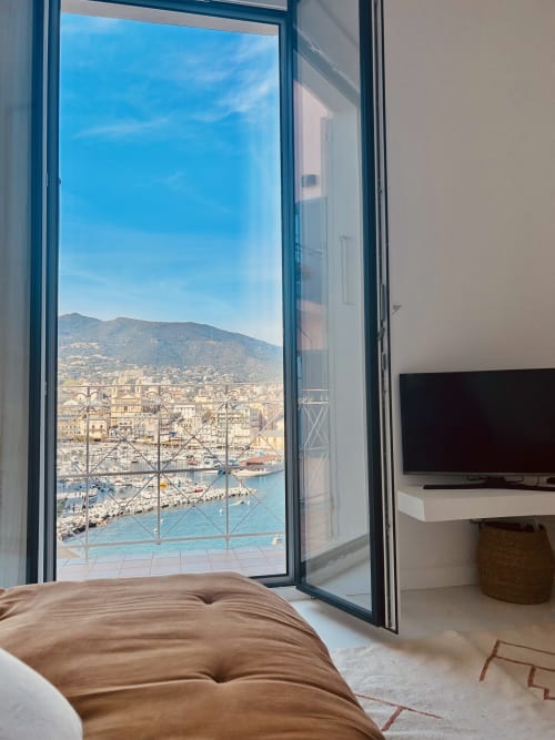 Bastia apartment balcony view overlooking Mediterranean harbor, mountains, and seaside town from bedroom with TV