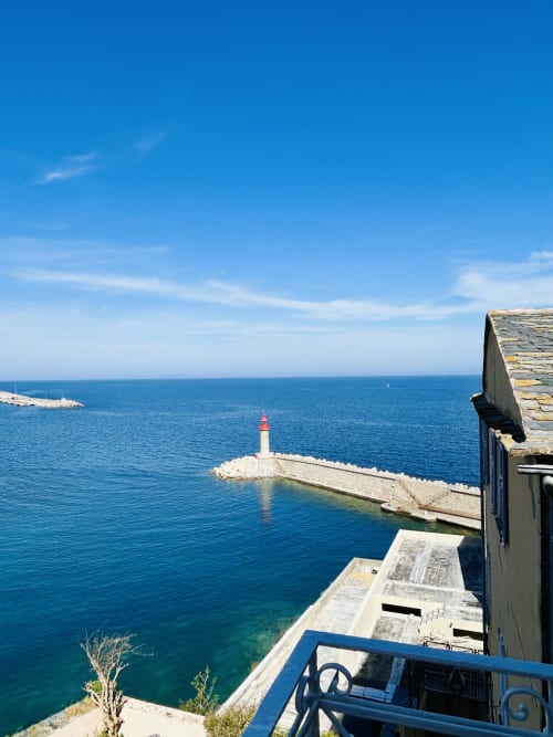 Bastia harbor view from Casa di Bastia balcony with red lighthouse, stone pier, and Mediterranean Sea
