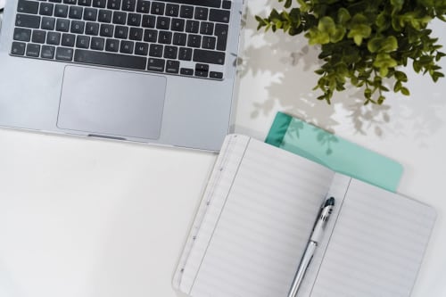 Spazio di lavoro ad AmazHome Rimini: laptop, quaderno con penna e pianta verde su scrivania bianca