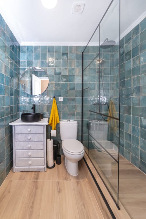 Casa de banho moderna no Bica Mini Hostel Lisboa com azulejos azul-turquesa, lavatório vessel preto, sanita e duche integrado