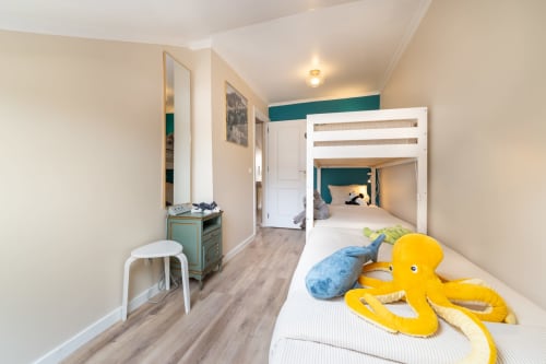 Quarto de albergue em Lisboa com beliches brancos, polvo amarelo, parede em tons de verde-azulado, espelho e piso de madeira.