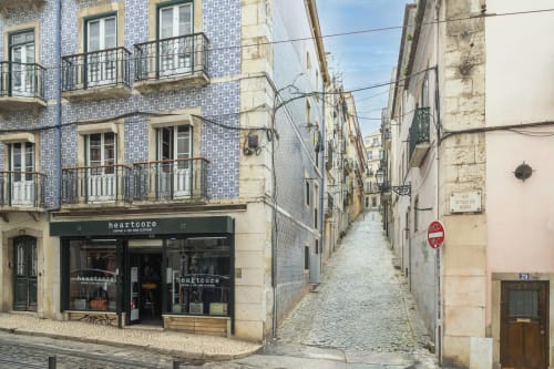 Rua histórica de Lisboa com edifício revestido de azulejos azuis abrigando a loja Heartcore perto do Bica Mini Hostel