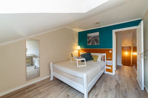 Quarto moderno no apartamento do Bica Mini Hostel Lisboa com cama branca, parede de destaque em azul-turquesa, pisos de madeira e casa de banho privativa