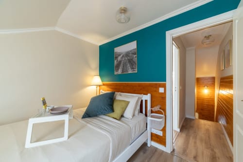 Quarto moderno no Bica Mini Hostel em Lisboa com parede de destaque azul-petróleo, cabeceira em madeira e acesso a casa de banho privativa