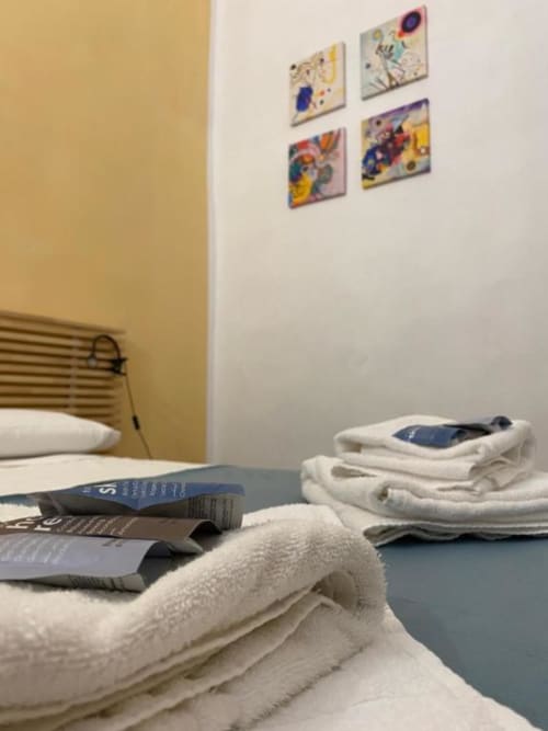 Camera accogliente presso Bronze Horse Affittacamere a Firenze con asciugamani bianchi, libri e quadri colorati alle pareti