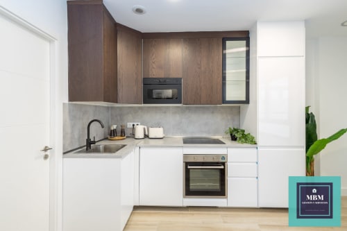 Cocina moderna en dúplex MBM, Arucas, con mueblería blanca y madera, electrodomésticos acero inoxidable y gris