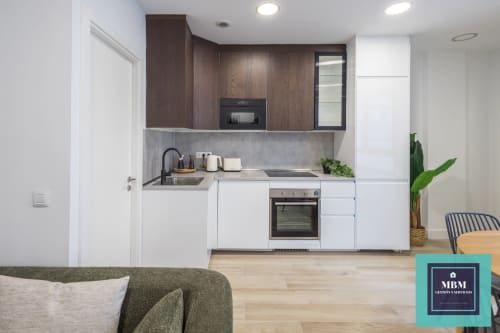 Cocina moderna del apartamento Dúplex Albareda en el hostel MBM, Arucas con muebles blancos, armarios superiores de madera oscura y área de estar
