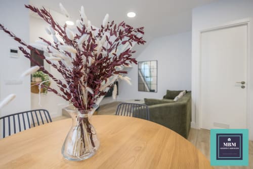 Comedor moderno con mesa de madera, flores secas burdeos en jarrón transparente y sofá verde en apartamento MBM Duplex, Arucas
