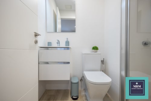 Baño moderno en apartamento dúplex MBM, Arucas Las Palmas, con tocador blanco, inodoro, espejo y decoración con planta verde