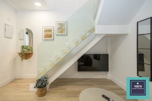 Sala de estar moderna en dúplex de MBM Arucas con escalera, televisor, pisos de madera y vista a la ciudad