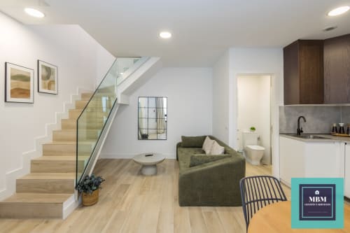 Moderno dúplex de concepto abierto en MBM Arucas con escaleras de madera, sofá verde, cocina, baño y vistas a la ciudad