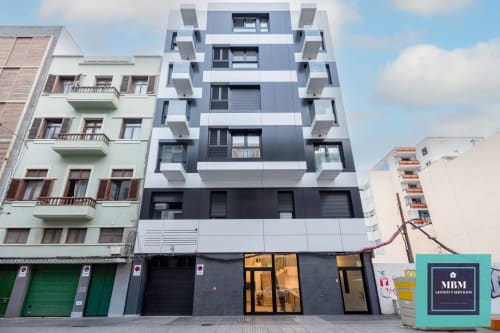 Exterior del albergue MBM en Arucas, Las Palmas - moderno edificio de apartamentos gris con balcones y local comercial en planta baja