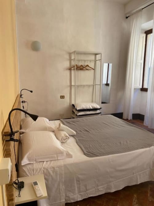 Bright bedroom at Bronze Horse Affittacamere in Florence with queen bed, shelving, bicycle, and windows with sheer curtains