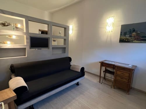 Modern studio apartment in Padova featuring black sofa, built-in shelving with TV, wooden desk, and contemporary lighting