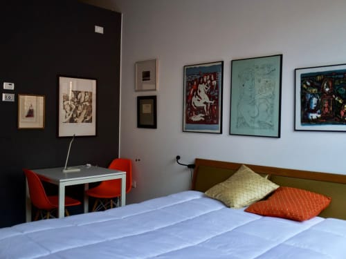 Modern bedroom at Il Maestrale B&B in Padova with bed, desk, red chairs, and framed artwork on walls