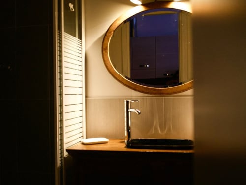 Modern bathroom vanity with wooden countertop, contemporary faucet, and round mirror with wooden frame at Il Maestrale B&B in