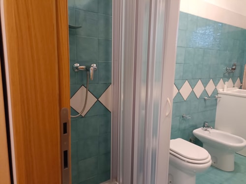 Bagno moderno con piastrelle turchesi, wc e bidet bianchi, cabina doccia e porta arancione presso Tales of Abruzzo