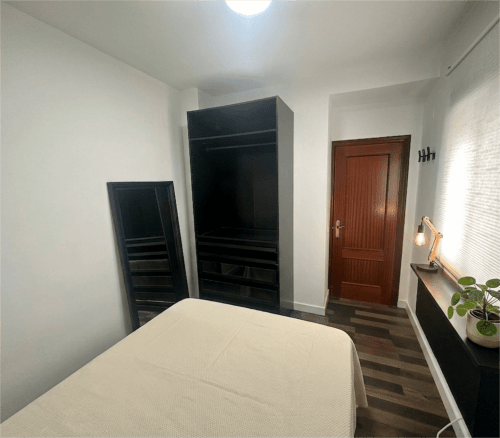 Dormitorio moderno en apartamentos Living Sur de Sanlúcar de Barrameda con cama, armarios negros y puerta de madera