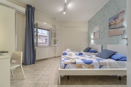 Camera da letto moderna a Messina con letto matrimoniale, biancheria blu, opere d'arte costiera, finestra con vista sul giardino e stile contemporaneo