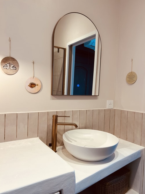 Modern bathroom in Casa di Bastia with white vessel sink, bronze faucet, arched mirror and coastal décor in Bastia, France