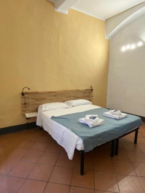 Camera minimalista al Bronze Horse Affittacamere di Firenze con pareti gialle, letto in legno e asciugamani piegati sul