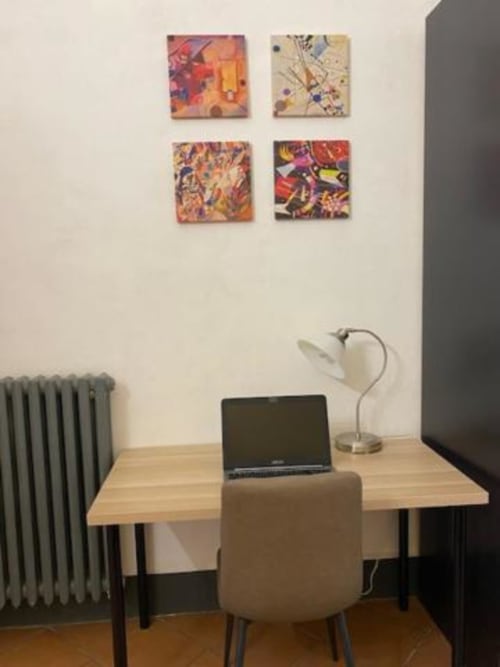 Espacio de trabajo moderno en Bronze Horse Firenze con laptop, lámpara de escritorio, arte mural colorido y radiador en habitación de B&B en Florencia