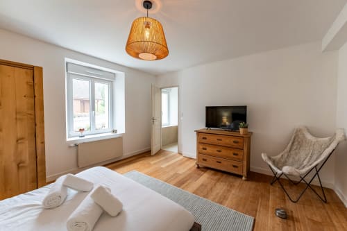 Chambre moderne au Refuge des Brumes avec mobilier en bois, linge blanc, télévision et éclairage suspendu
