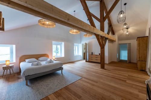 Chambre spacieuse à Le Refuge des Brumes avec poutres apparentes, murs blancs, plancher bois et luminaire moderne